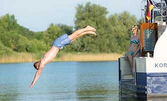 ein junger Mann springt von der Badeplattform des Hausbootes Kormoran in den See Müritz