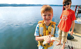 Zwei kleine Angler auf einem Hausboot zeigen stolz einen Fisch.